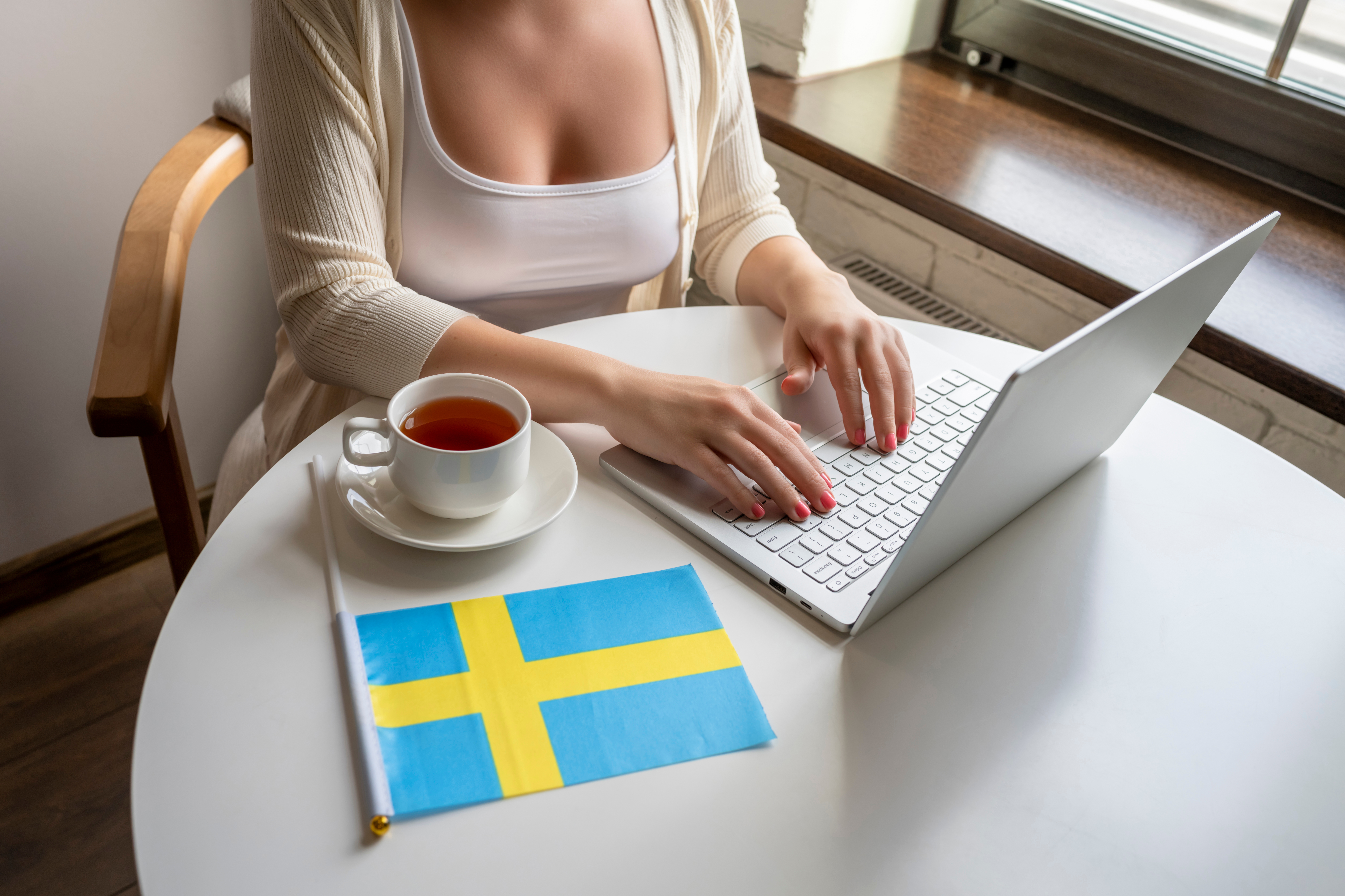 Девушка с ноутбуком возле флага Швеции, страны, работа в которой доступна для иностранцев